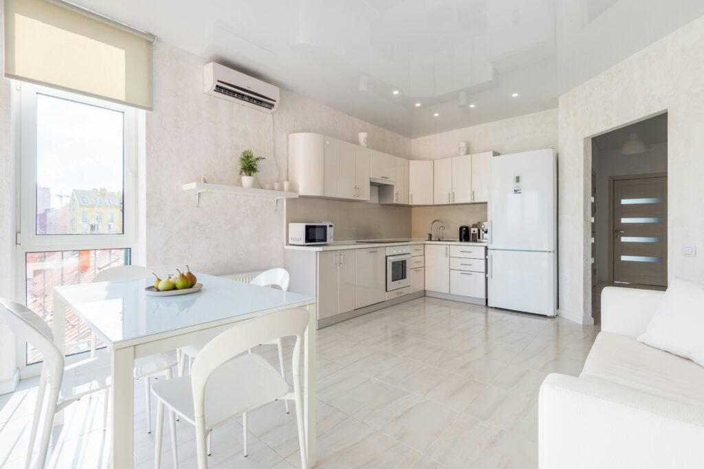 Spacious contemporary kitchen interior featuring white furniture, appliances, and natural light.